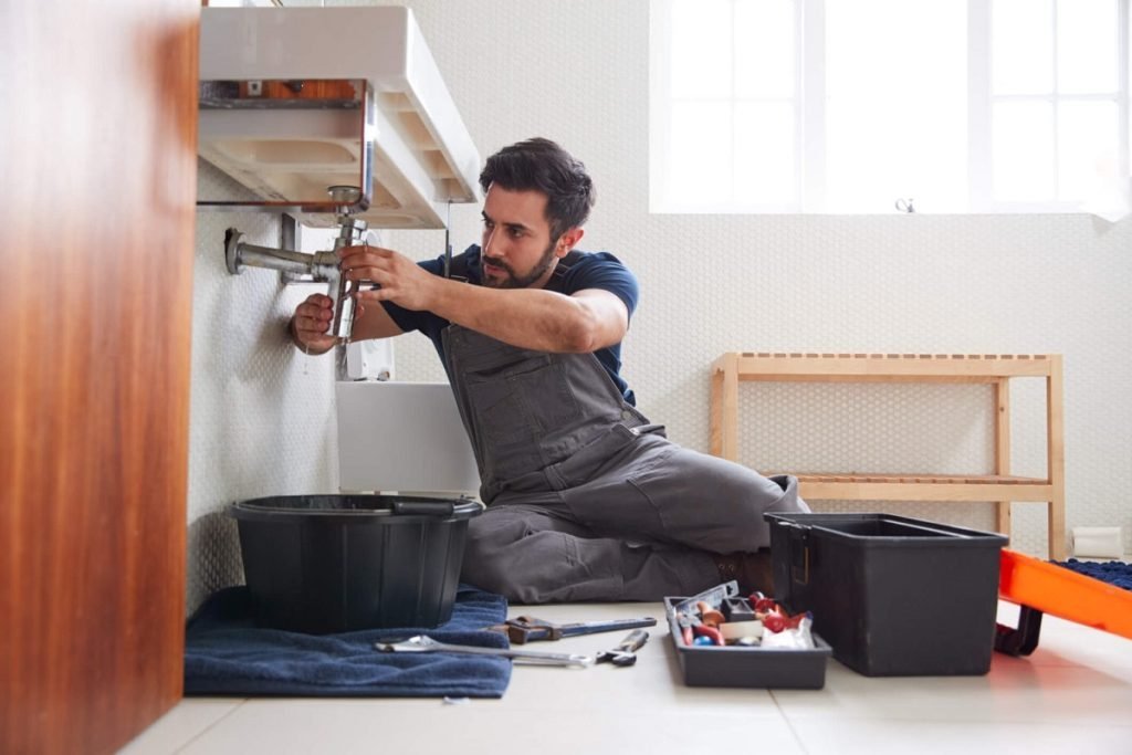 Plumber on bathroom floor fitting the drain trap under a wall-mounted sink