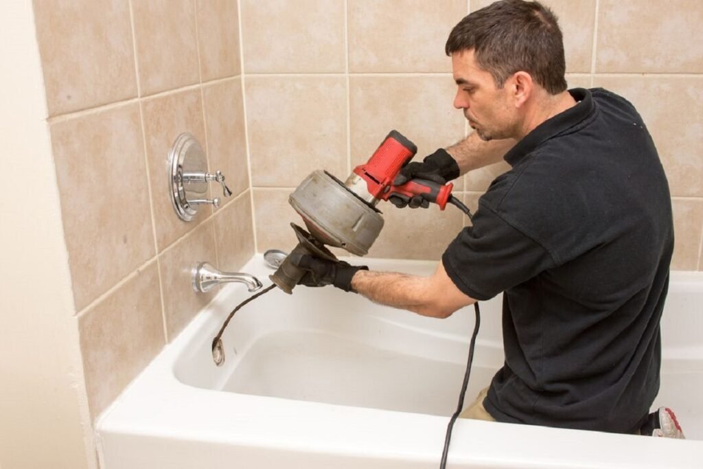 Plumber clearing a bathtub drain with a powered drain auger