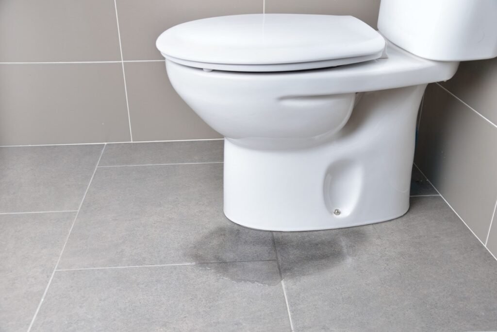Water pooling on grey tile floor beside a leaking white toilet