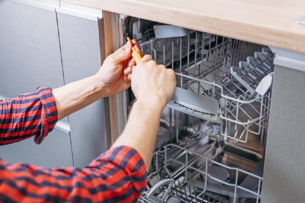 Hands using a screwdriver to secure a built-in dishwasher under a counter