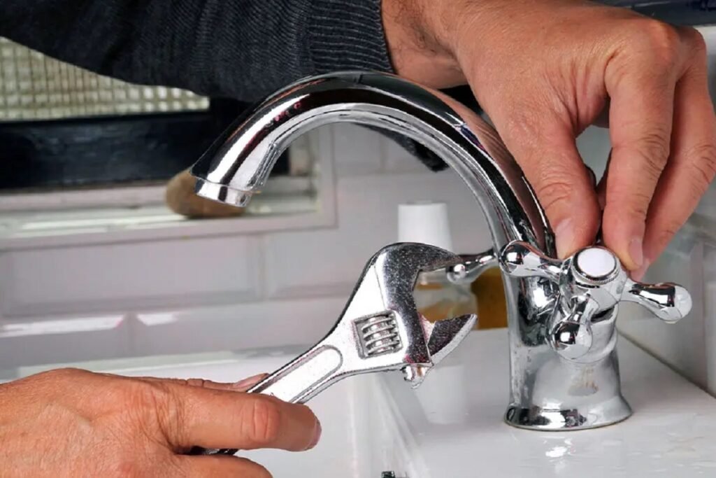 Hands tightening a chrome sink faucet with an adjustable wrench