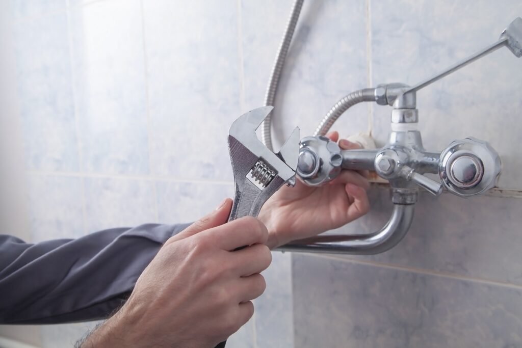 Plumber tightening a chrome tub and shower faucet with an adjustable wrench