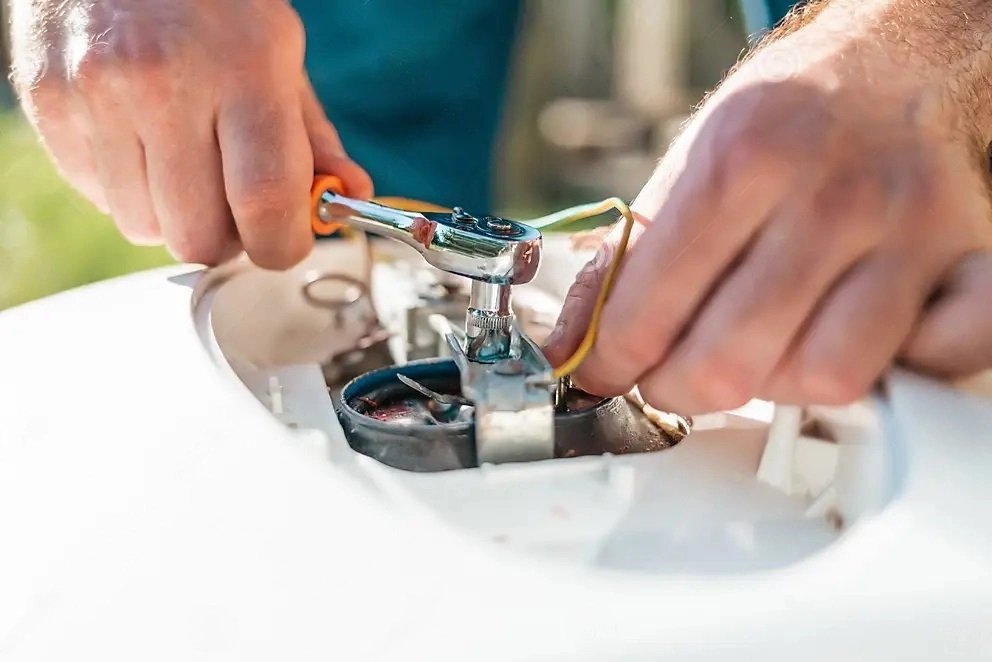 Hands using a ratchet wrench inside an open water heater access panel
