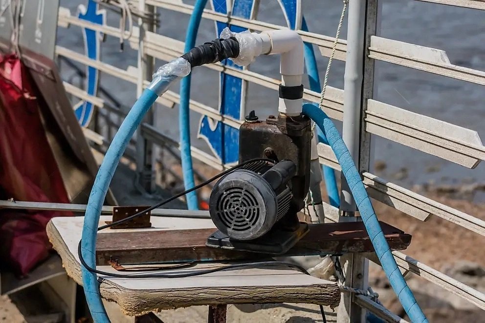 Electric water pump with blue hoses and PVC piping mounted on a wooden board