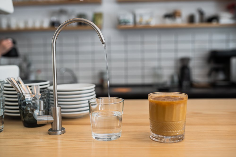 Filtered water pouring from a slim tap into a glass on a counter