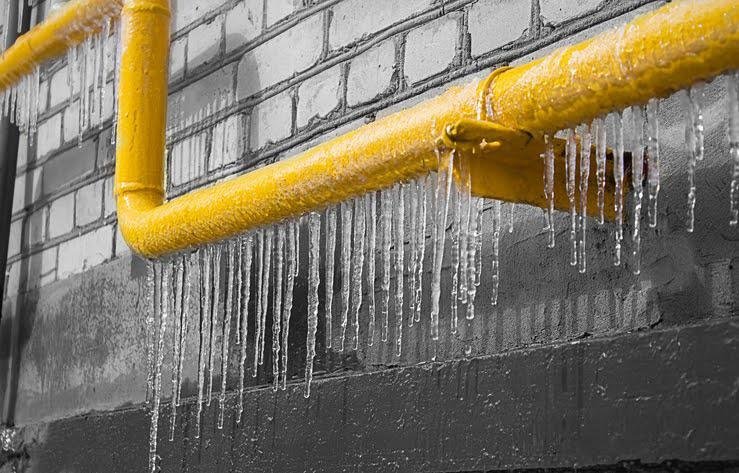 Icicles hanging from a frozen yellow pipe along a brick wall
